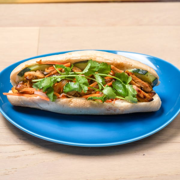 A banh mi sandwich with grilled chicken, pickled carrots, cucumbers, and cilantro on a blue plate.