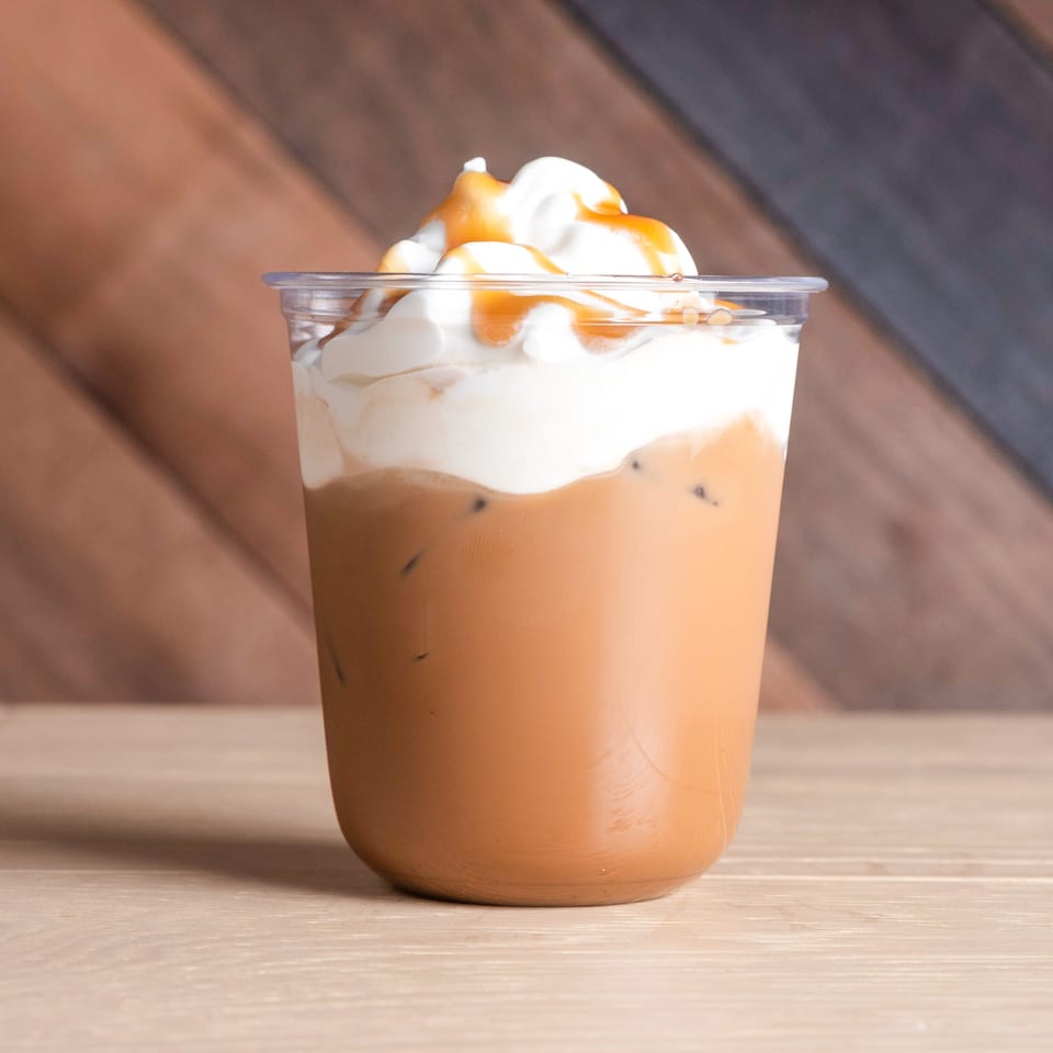 Iced coffee with whipped cream and caramel drizzle in a clear plastic cup.