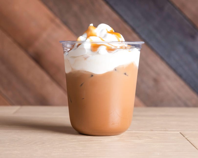 Iced coffee with whipped cream and caramel drizzle in a clear plastic cup.