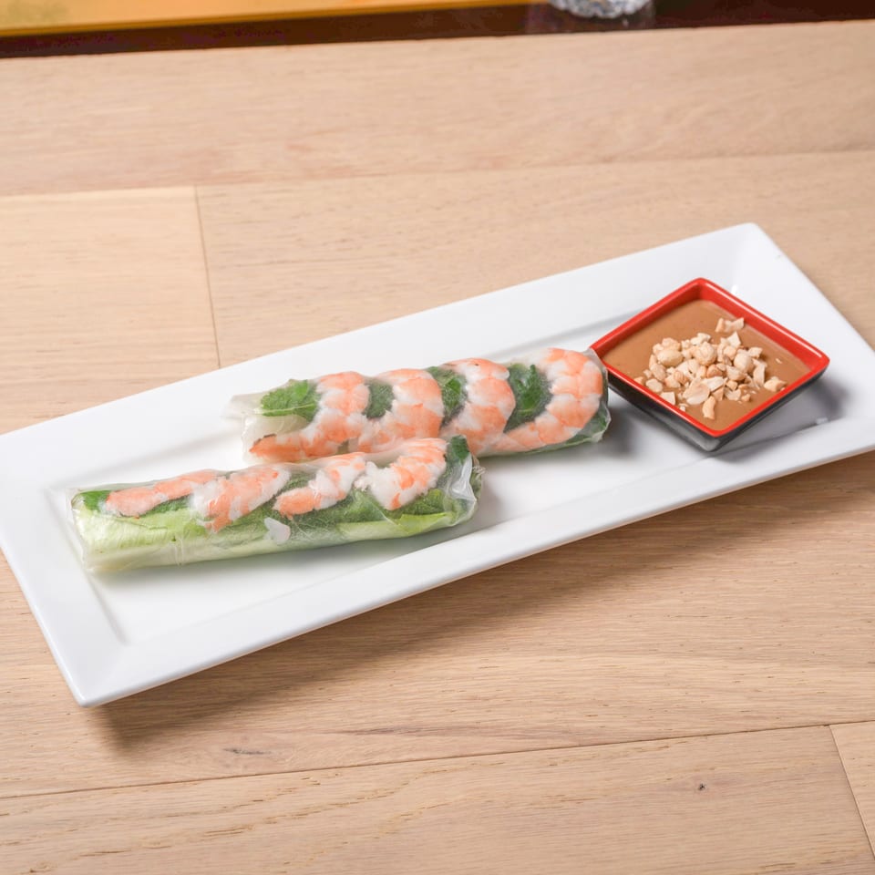 Two fresh shrimp spring rolls with lettuce and herbs, served with peanut dipping sauce on a white plate.