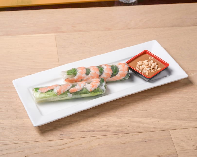 Two fresh shrimp spring rolls with lettuce and herbs, served with peanut dipping sauce on a white plate.